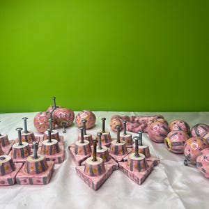 May include: A collection of pink and yellow ceramic cabinet knobs and pulls. The knobs are round and the pulls are oblong. The knobs and pulls have a decorative design with silver hardware. The knobs and pulls are for furniture.