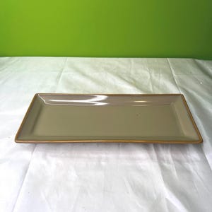 May include: A rectangular serving tray with a light brown glaze and a gold rim.