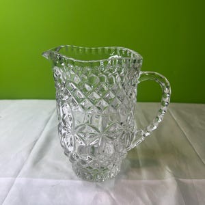 Puede incluir: Una jarra de vidrio transparente con un patrón de diamante. La jarra tiene un asa y una boca ancha.