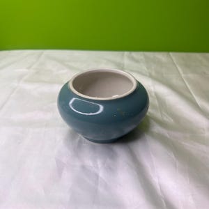 May include: A small, round, teal ceramic planter with a white interior.