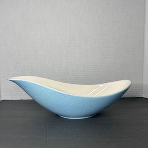 Könnte beinhalten: Eine hellblaue Keramikschale mit weißem Überzug und einem wellenförmigen Design. Die Schale ist leicht geschwungen und hat eine strukturierte Oberfläche.
