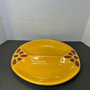 May include: A yellow ceramic serving dish with two divided sections. The dish has a brown and red floral design around the edges.