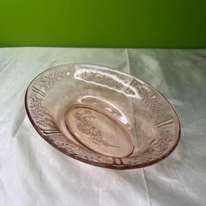 May include: Pink oval glass serving dish with floral etched detailing. The dish has a raised rim and a central floral design. The glass has a slight pink hue and is set against a white background.