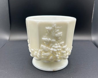 May include: White milk glass vase with a grapevine design. The vase has a scalloped rim and a pedestal base.