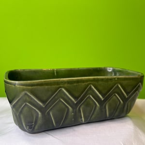 May include: A dark green ceramic planter with a geometric design. The planter is rectangular and has a slightly rounded bottom.