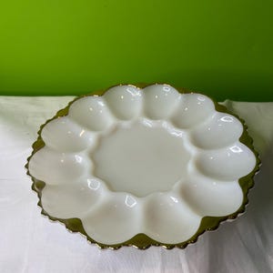 Peut inclure: Plat à œufs en verre laiteux blanc avec un bord doré. La plaque comporte 10 indentations individuelles pour contenir des œufs.
