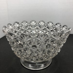 May include: A clear glass bowl with a scalloped edge and a diamond pattern. The bowl has a pedestal base.