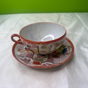 Peut inclure: Un service à thé vintage composé d'une tasse et d'une soucoupe. La tasse et la soucoupe ont un intérieur blanc et un bord rouge. L'extérieur présente un motif détaillé et coloré d'inspiration asiatique avec des personnages et des éléments floraux.