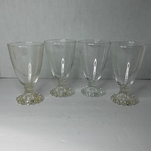 May include: Four clear glass goblets with a beaded base. The goblets are empty and have a classic design.