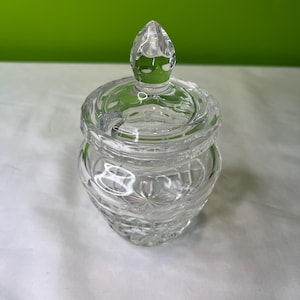 Puede incluir: Un tarro de vidrio transparente con un diseño de corte de cristal y una tapa puntiaguda. El tarro está vacío y tiene un acabado liso y pulido.