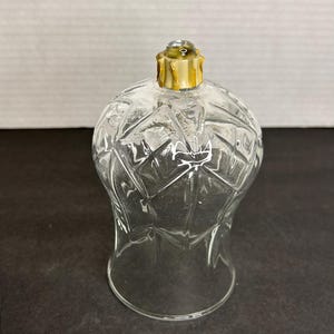 Puede incluir: Un portavelas de vidrio transparente con un patrón geométrico y una parte superior dorada.