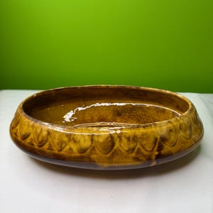 May include: A brown ceramic bowl with a scalloped edge. The bowl has a glossy finish and a dark brown interior. The exterior is a lighter shade of brown with a textured pattern. The bowl is oval-shaped and sits on a white surface.
