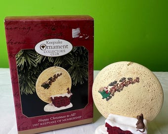 May include: A white ceramic Christmas bauble featuring Santa Claus and his reindeer flying over a moon with a chimney and a cat on the roof. The bauble is packaged in a red box with the text "Keepsake Ornament Collector's Club" and "Happy Christmas to All! 1997 Keepsake of Membership".