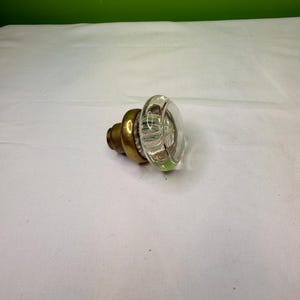 May include: A clear glass doorknob with a brass base. The glass portion is round with vertical ridges, and the brass base has a stepped design. The doorknob is a vintage style.