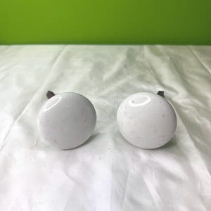 May include: Two white ceramic knobs with a speckled finish. The knobs are round and have a small hole in the center for mounting.
