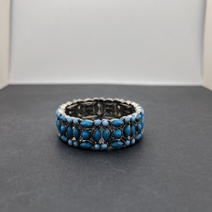 May include: A stretch bracelet featuring rows of marquise-shaped and round turquoise-coloured cabochons set in a dark, antiqued silver-tone metal frame. The design consists of three horizontal bands of stones arranged in a repeating pattern.