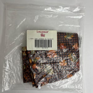 May include: A plastic bag containing a set of four brown and orange fabric liners with a gingham pattern and a fall leaf design. The bag has a label that reads "Longaberger Liner - 1997 Shades of Gingham".