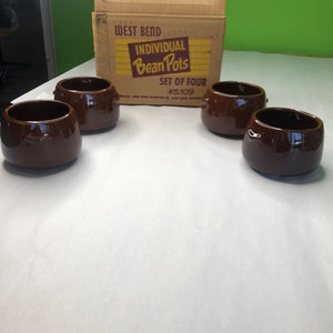 May include: A set of four brown ceramic bean pots with handles. The pots are in a cardboard box that says "West Bend Individual Bean Pots Set of Four #5109".
