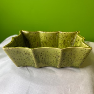 May include: A green ceramic planter with a starburst shape and a speckled glaze.