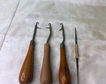 May include: Three crochet hooks with wooden handles and a single needle tool. The hooks have metal tips and are labeled "MADE IN KOREA" and "MADE IN USA". The tools are arranged on a white surface.