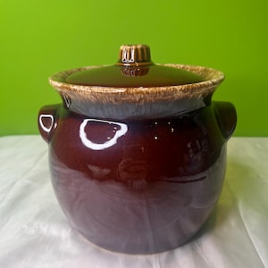 May include: A brown ceramic crock with a lid. The crock has a glazed finish and a white rim. The lid has a knob on top.