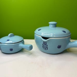 Può includere: Set di stoviglie in ceramica blu chiaro in due pezzi. Il set include una piccola ciotola con coperchio e una ciotola più grande con manico e beccuccio. Entrambi i pezzi hanno disegni floreali blu scuro e coperchi abbinati.