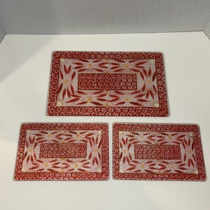 Puede incluir: Juego de tres manteles individuales de vidrio rojo y blanco con diseño floral. Los manteles individuales son rectangulares y tienen un borde alrededor del borde.