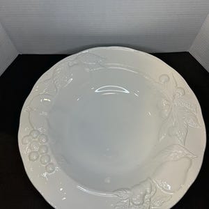 Op de afbeelding: Witte keramische serveerschaal met een reliëf van fruit en bladeren rond de rand.