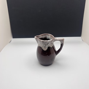 Może przedstawiać: Mały brązowy dzbanek do śmietanki z białą glazurą. Dzbanek ma zaokrąglone ciało i mały uchwyt.