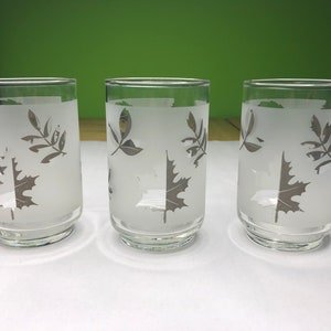 May include: Three frosted glass tumblers with a silver leaf design. The glasses are clear and have a frosted finish. The leaves are etched into the glass and are a silver color.