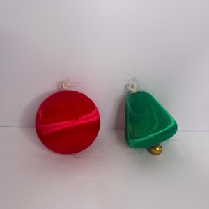 May include: Two Christmas ornaments: a red sphere and a green bell. The sphere is a solid red color. The bell has a gold-colored clapper. Both ornaments have a loop for hanging.