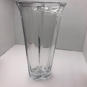 May include: A clear glass vase with a tall, slender shape and a slightly flared opening. The vase has a faceted design, creating a geometric pattern.