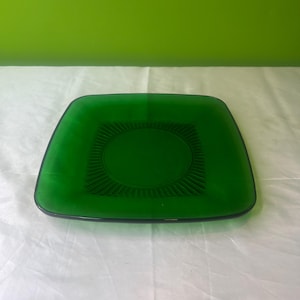Può includere: Un piatto quadrato di vetro verde con un motivo decorativo attorno al centro.