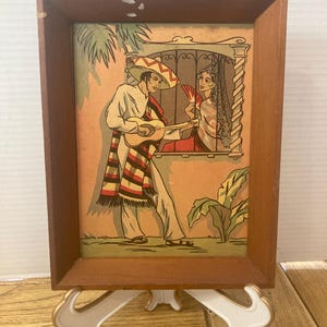 May include: A rectangular wooden frame containing a vintage-style illustration of a person in a sombrero playing a guitar for another person looking out of a window. The scene features palm leaves, a striped serape, and a hand-held fan in warm tones.