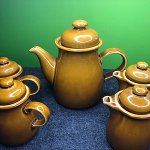 Può includere: Un set di cinque teiere in ceramica marrone con coperchi. Le teiere sono disposte su una superficie grigia.