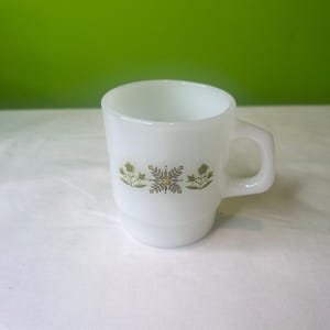 Puede incluir: Taza de cerámica blanca con un diseño floral verde y amarillo. La taza tiene un asa y es de tamaño estándar.