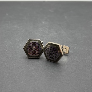 May include: A pair of hexagonal cufflinks featuring a metallic finish with a repeating honeycomb pattern in shades of purple and black. The cufflinks have a polished silver-tone metal border and a standard hinged toggle mechanism on the back.