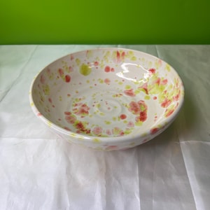 May include: A white ceramic bowl with a speckled pink and green glaze. The bowl is round and has a slight lip.
