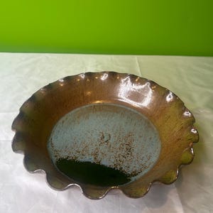 Puede incluir: Un plato para tartas de cerámica marrón con un borde festoneado y un glaseado azul y verde.