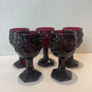 May include: Set of five ruby red glass wine goblets with a detailed embossed pattern. The goblets have a hexagonal base.