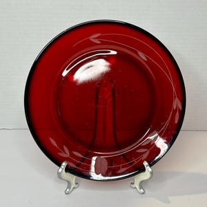 May include: A red glass dinner plate with a white etched design of leaves and swirls around the rim.