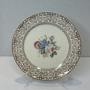 Könnte beinhalten: Ein weißer Keramik-Dinnerteller mit goldfarbenem Rand und einem floralen Design in der Mitte. Die Blumen sind rosa, weiß, blau und gelb.