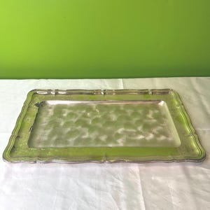 Op de afbeelding: Een zilveren dienblad met een decoratieve, gegolfde rand. Het dienblad heeft een licht getextureerd oppervlak en is rechthoekig.