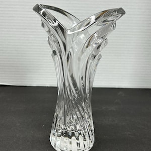 May include: A clear glass vase with a swirling, textured design. The vase has a wide, open mouth and a narrow base.