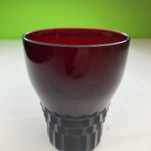 May include: A dark red glass tumbler with a fluted base. The glass is clear and has a smooth, polished finish.