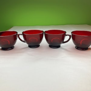 Peut inclure: Ensemble de quatre tasses à thé en verre rouge avec des poignées. Les tasses sont disposées en rangée sur une surface blanche.