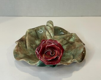 May include: A green ceramic dish with a ruffled edge and a twisted rope handle. A red rose is attached to the handle.