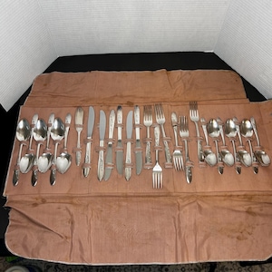 May include: A set of vintage silverware in a brown leather roll. The silverware includes spoons, forks, and knives. The silverware is in a roll with a brown leather exterior.
