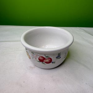 Peut inclure: Bol en céramique blanc avec un bord arrondi. Le bol est décoré d'un motif de fruits avec des pommes rouges, des myrtilles et d'autres fruits et fleurs colorés. Le bol est adapté pour servir des aliments.