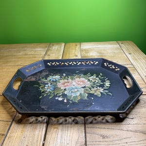 May include: Vintage black metal serving tray with a floral bouquet design in shades of pink, blue, and white. The tray has a decorative cut-out border and handles on each side. The tray is octagonal in shape.